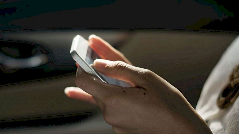 A person is holding and using a smartphone, possibly texting or browsing, inside a dimly lit car.