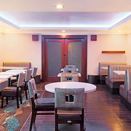 The image shows a modern dining area with booth seating, cushioned chairs, and white tables arranged in a well-lit room with wooden and tiled flooring.