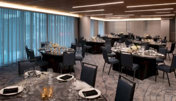The image shows a banquet hall set for an event, with round tables adorned with black linens, chairs neatly arranged, and centerpieces on each table.