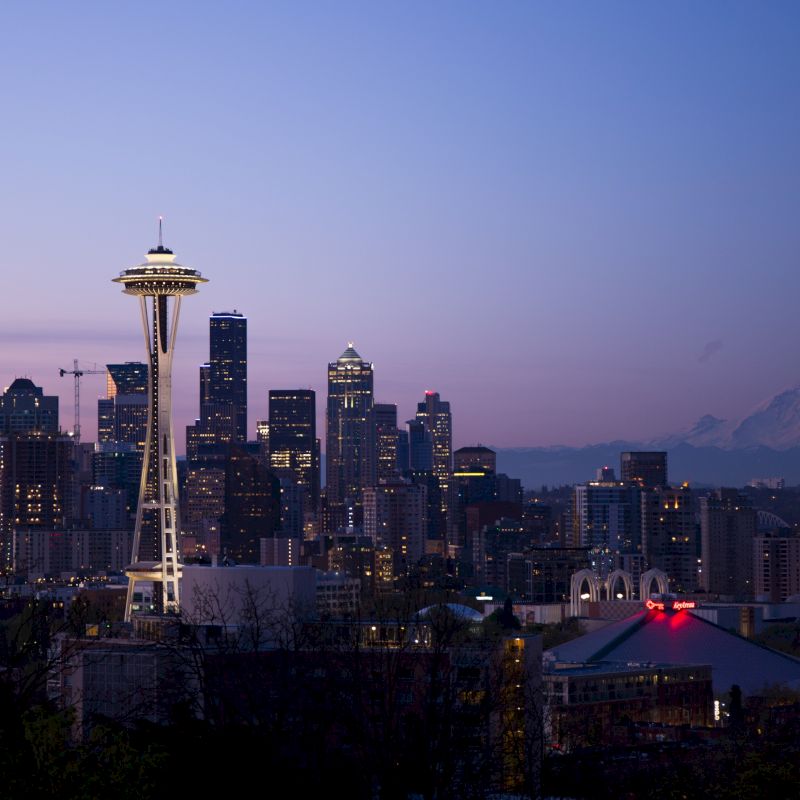 This image shows a dusk skyline of Seattle, with the iconic Space Needle prominently featured and Mount Rainier visible in the background.