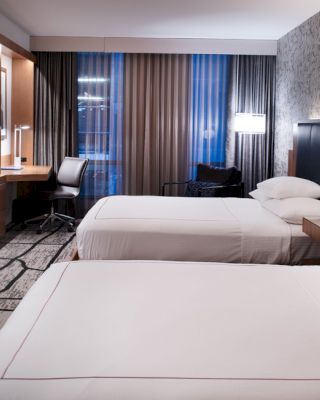 A modern hotel room features two beds, a flat-screen TV, a desk with a chair, and stylish decor.