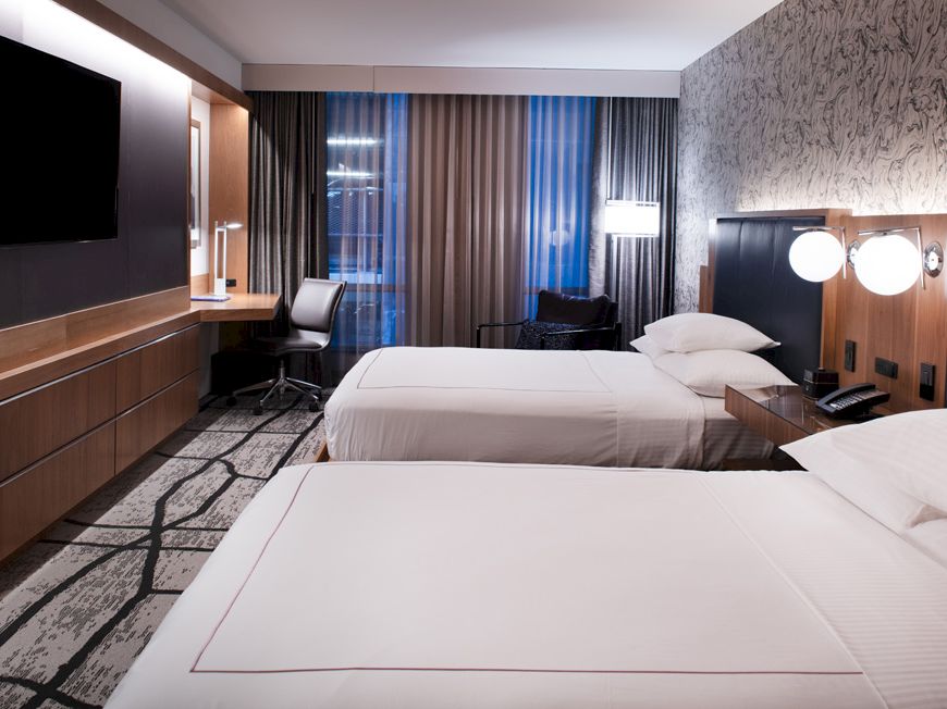 A modern hotel room with two beds, a TV, a desk with a chair, and artistic wallpaper.