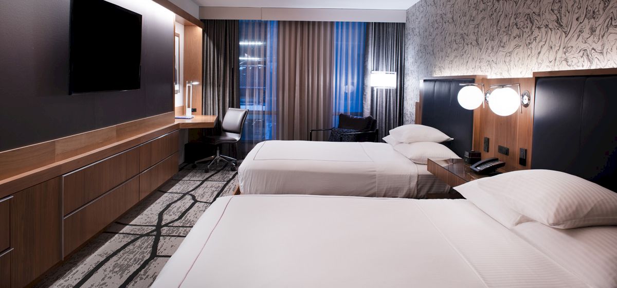 A modern hotel room with two beds, a TV, a desk with a chair, and artistic wallpaper.