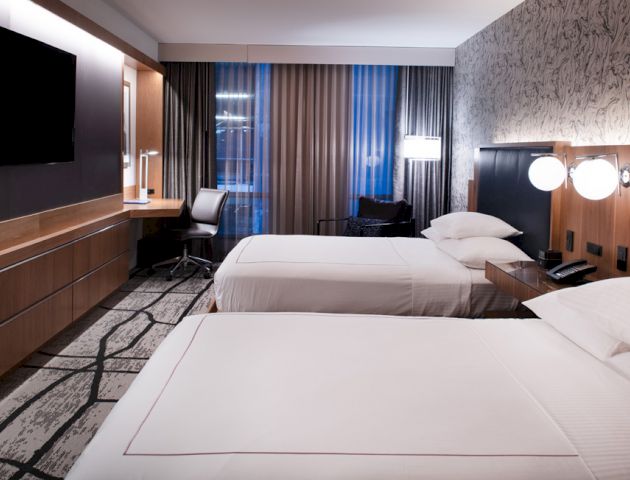 The image shows a modern hotel room with two neatly made beds, a flat-screen TV, a work desk by the window, and contemporary decor ending the sentence.