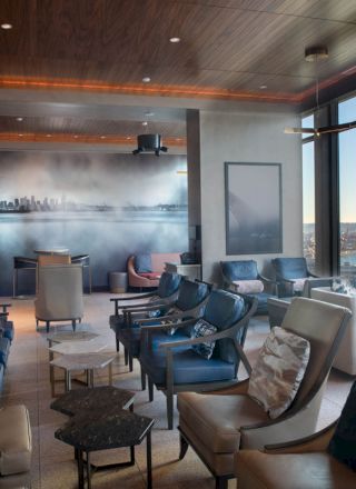 A modern lounge with comfortable seating, large windows offering a scenic view, and a cityscape mural on the wall.