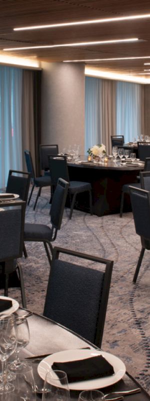 A banquet hall with several round tables covered in dark tablecloths, set for a formal event with chairs, glassware, and centerpieces, under modern lighting.