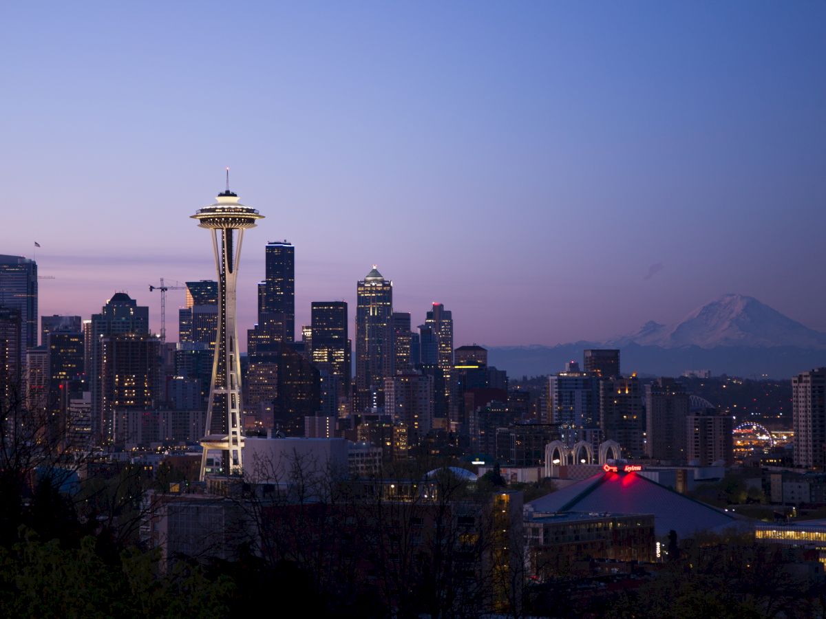 The image features a twilight view of Seattle's skyline, prominently showcasing the Space Needle with Mount Rainier visible in the distance.