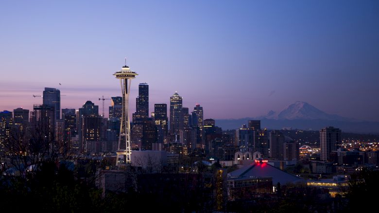 The image features a twilight view of Seattle's skyline, prominently showcasing the Space Needle with Mount Rainier visible in the distance.