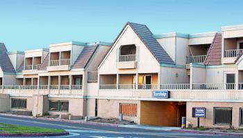 The image shows a two-story, beige colored building with brown roofs, labeled 